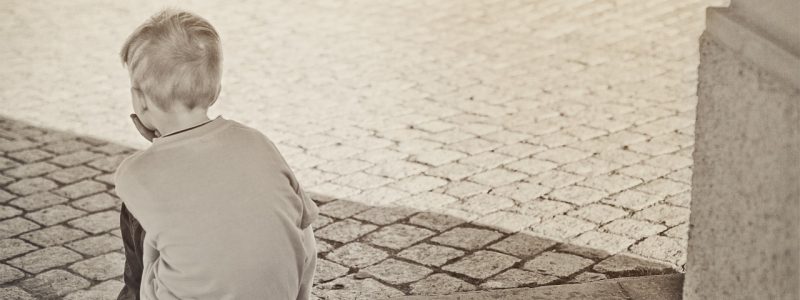 black and white image of disappointed little boy sitting on steps