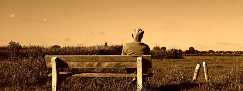 Sepia image of an old man sittingon a bench and looking over the countryside